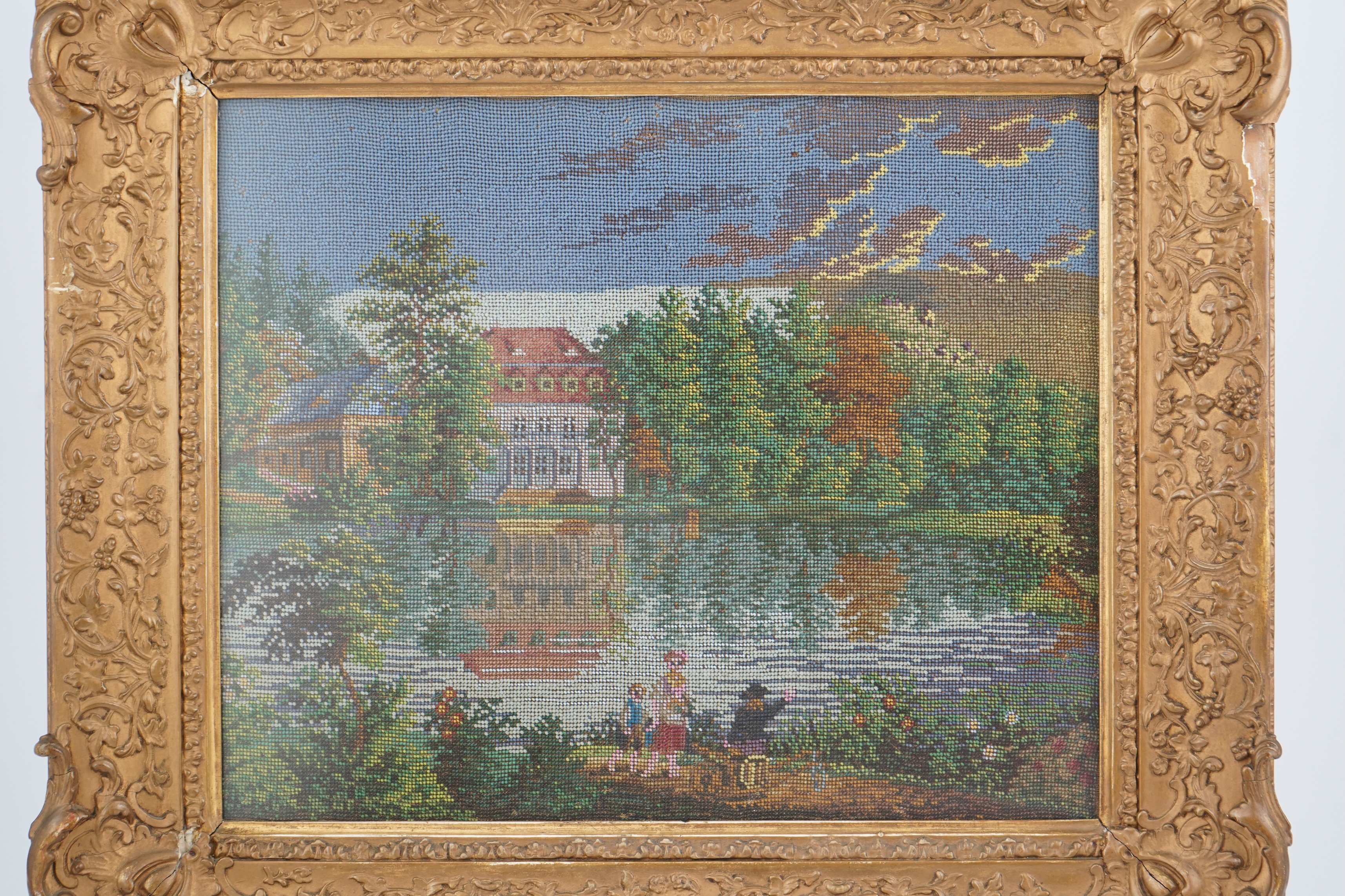 A 19th century framed Berlin beadwork panel, possibly German, country scene of a family walking along a garden path, away from a large lake and mansion surrounded by a forest of fire trees. 26cm wide x 30cm high. Conditi